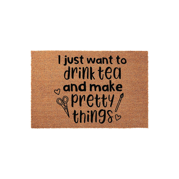 Crafting themed coir doormat featuring the text I just want to drink tea and make pretty things in black ink, accented with small heart, scissors, and paintbrush illustrations on a natural brown textured fiber background for a