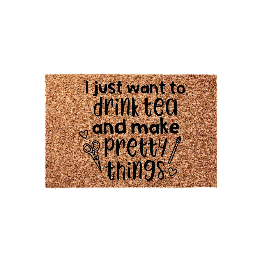 Crafting themed coir doormat featuring the text I just want to drink tea and make pretty things in black ink, accented with small heart, scissors, and paintbrush illustrations on a natural brown textured fiber background for a