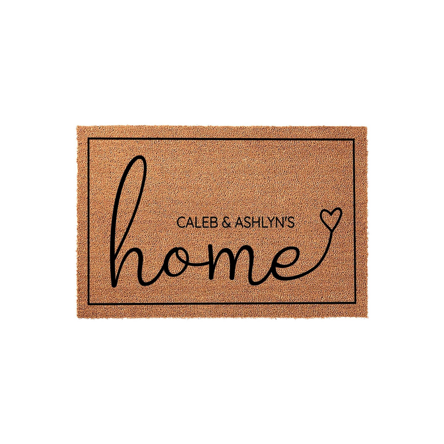 Personalized coir doormat featuring the word home in elegant black script with a heart accent, designed for a custom family entrance. This durable natural fiber welcome mat includes a thin black border and space for custom names.