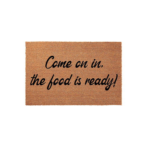 Come on in the food is ready doormat featuring a natural brown coir texture and bold black cursive lettering that creates a welcoming entrance for your home, perfect for a kitchen or dining room entryway on a plain white