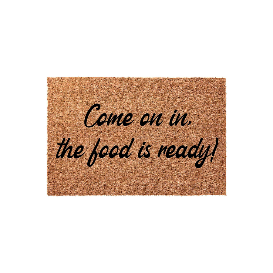 Come on in the food is ready doormat featuring a natural brown coir texture and bold black cursive lettering that creates a welcoming entrance for your home, perfect for a kitchen or dining room entryway on a plain white