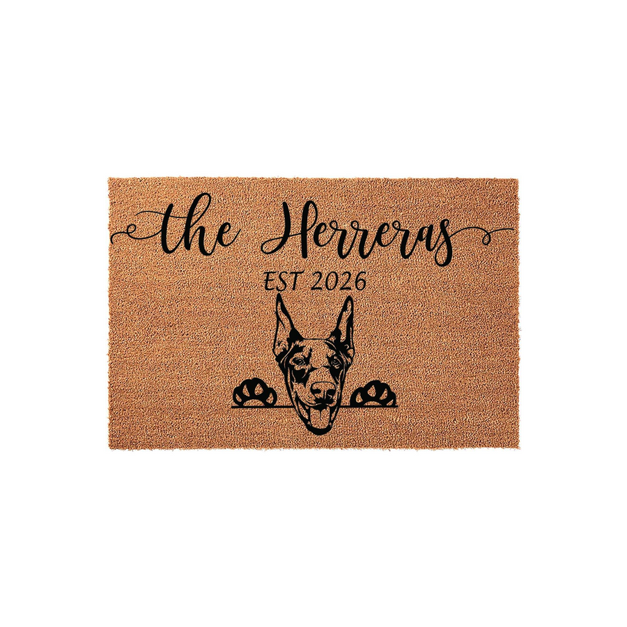 Personalized Doberman Pinscher doormat featuring a natural coir texture with a black printed illustration of a dog peeking over the edge, customized with a family name and established year on a clean white background.