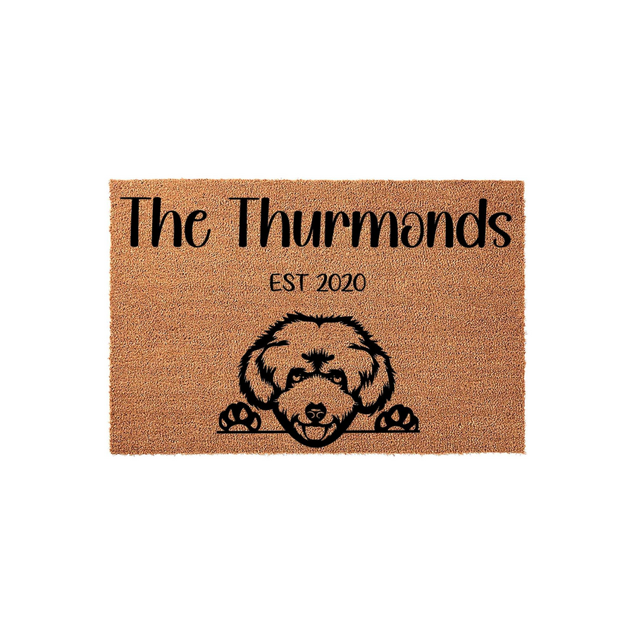 Personalized family name coir doormat featuring a cute doodle dog peeking over the bottom edge, with custom text and an established year printed in black ink on a natural brown textured fiber background for a welcoming home