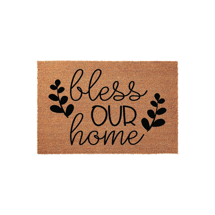 Bless Our Home coir doormat featuring black script lettering and simple leaf accents on a natural tan fiber background, creating a welcoming entryway decor piece for a front porch or house entrance that adds a touch of rustic