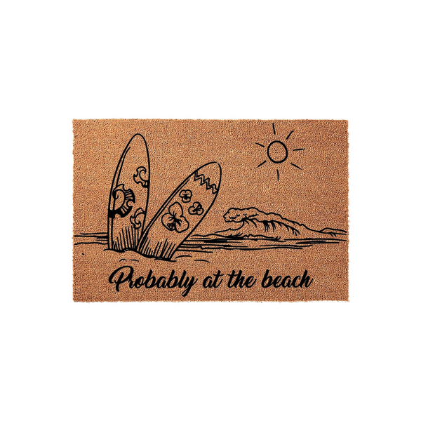 Probably at the beach coir doormat featuring a black line art illustration of two surfboards standing in the sand, a crashing ocean wave, and a bright sun, all set against a natural brown textured fiber background for a coastal