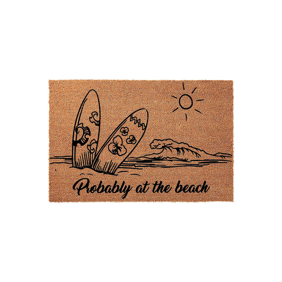 Probably at the beach coir doormat featuring a black line art illustration of two surfboards standing in the sand, a crashing ocean wave, and a bright sun, all set against a natural brown textured fiber background for a coastal