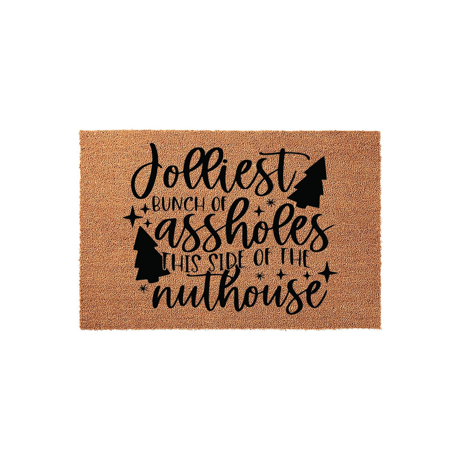 Funny Christmas doormat made of natural coir fiber, featuring black text that reads Jolliest Bunch of Assholes This Side of the Nuthouse with decorative pine tree silhouettes and stars on a plain white background for holiday home