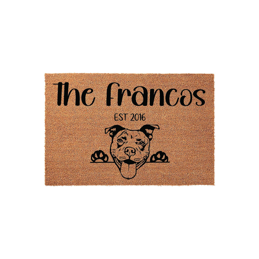 Personalized Pit Bull doormat featuring a cute dog illustration peeking over the edge, with custom family name text and established year printed in black on a natural coir fiber mat against a clean white studio background.