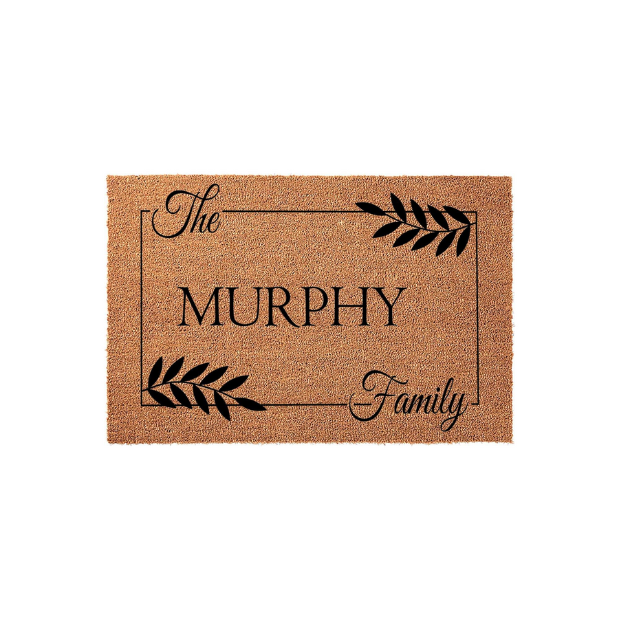 Personalized family name coir doormat featuring a rectangular border, elegant black script text, and decorative leaf accents on a natural brown textured fiber background, creating a welcoming entrance for any home front porch.