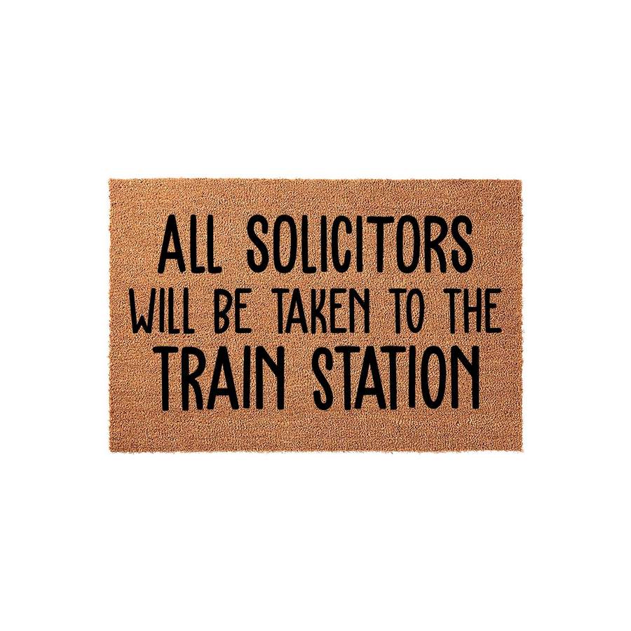 Funny Doormat with All Solicitors Will Be Taken To The Train Station text printed in bold black lettering on a natural tan coir fiber background, creating a humorous welcome mat for fans of western television shows and ranch life.