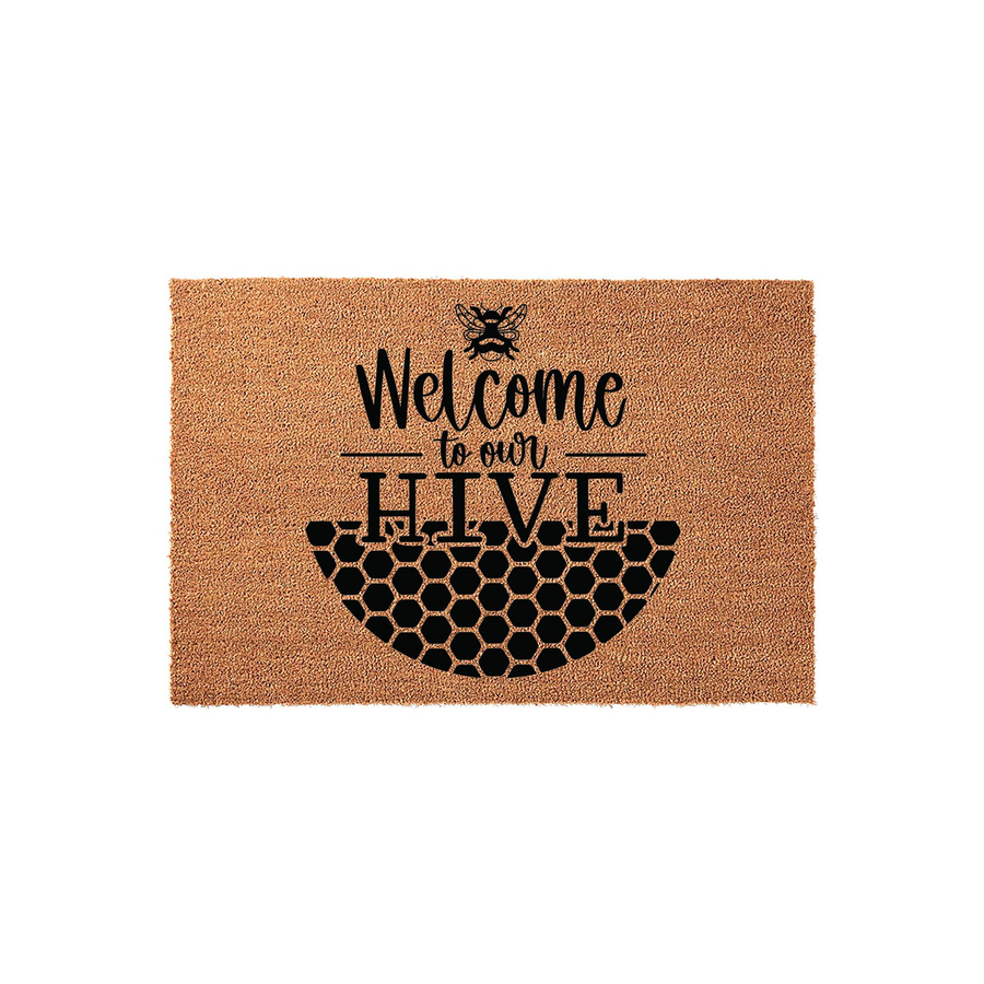 Bee Welcome to Our Hive Doormat featuring a natural coir texture with a black printed design of a honeybee, honeycomb pattern, and whimsical typography on a plain white background for a charming farmhouse entryway decor style.