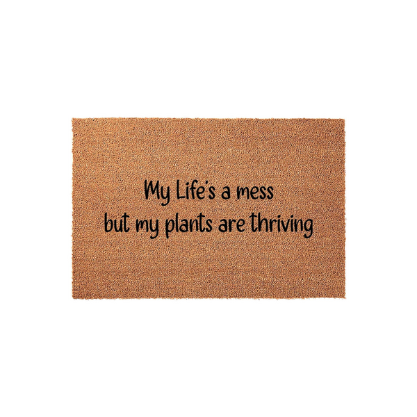 Funny Plant Lover Doormat featuring the text My Life's a mess but my plants are thriving printed in black script on a natural brown coir fiber mat, shown against a clean white background for a modern home entryway or porch decor.