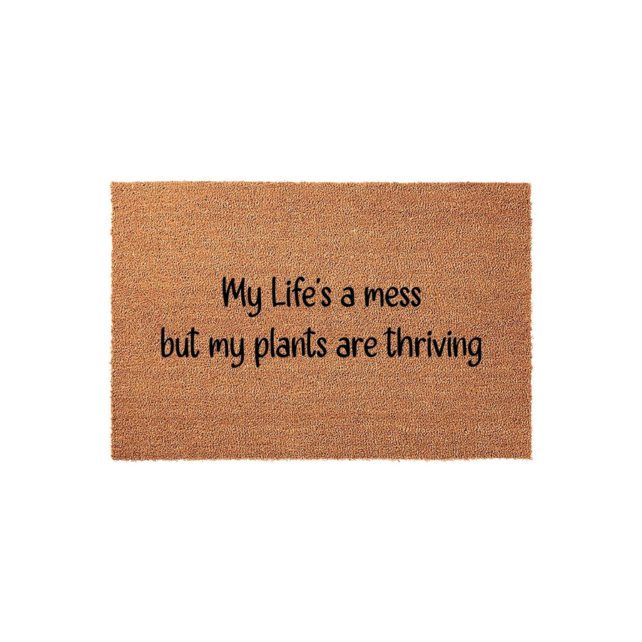 Funny Plant Lover Doormat featuring the text My Life's a mess but my plants are thriving printed in black script on a natural brown coir fiber mat, shown against a clean white background for a modern home entryway or porch decor.