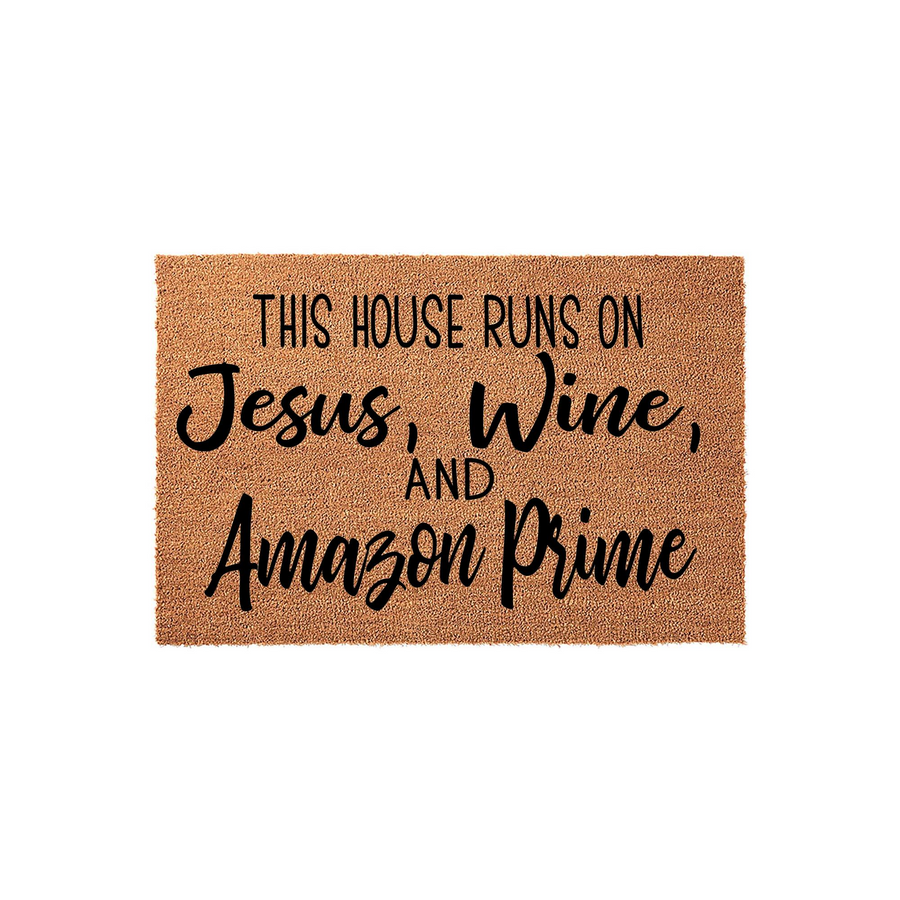 Funny Welcome Doormat featuring the text This House Runs On Jesus, Wine, And Amazon Prime printed in black ink on a natural tan coir fiber mat, creating a humorous and welcoming entryway decor piece for any modern home front