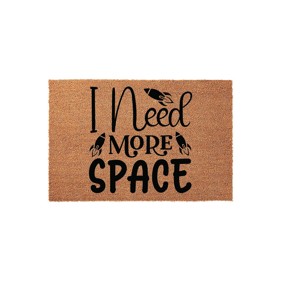 I Need More Space coir doormat featuring a fun outer space theme with black rocket ship graphics printed on a natural brown textured fiber background, creating a humorous welcome mat for any science fiction or astronomy