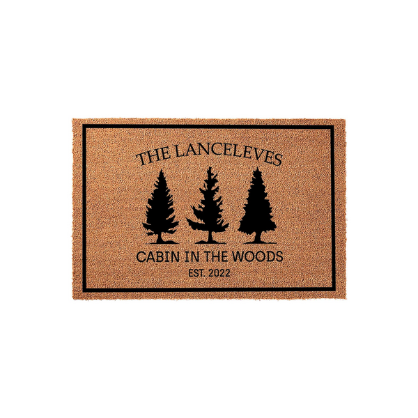 Personalized Cabin in the Woods doormat featuring a natural coir texture, black pine tree silhouettes, and custom family name text with an established year, all framed by a simple black border on a clean white studio background.