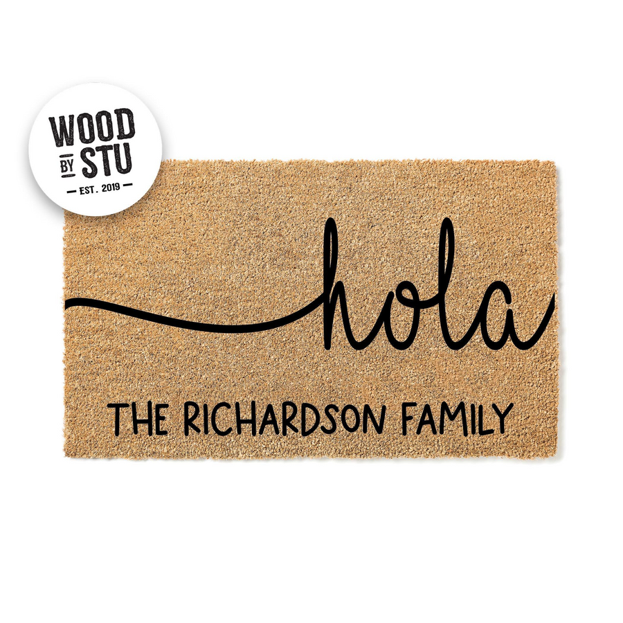 Personalized Hola doormat made of natural coir fiber, featuring a modern black script font that says hola above a custom family name line, creating a welcoming entrance for any home on a clean white background.