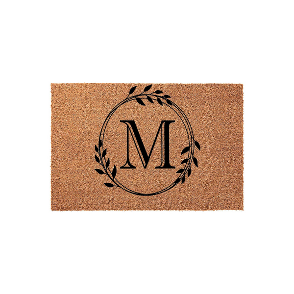 Personalized Monogram Coir Doormat featuring a large black letter M centered inside a delicate hand-drawn botanical leaf wreath, set against a natural tan textured coconut fiber background for a classic farmhouse entryway decor