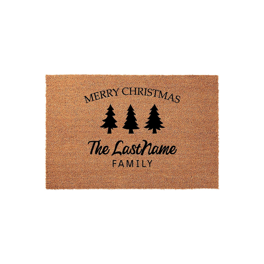 Personalized Merry Christmas coir doormat featuring three black pine tree silhouettes and custom family name text printed in a festive style, set against a plain white background for a clean holiday home decor look.