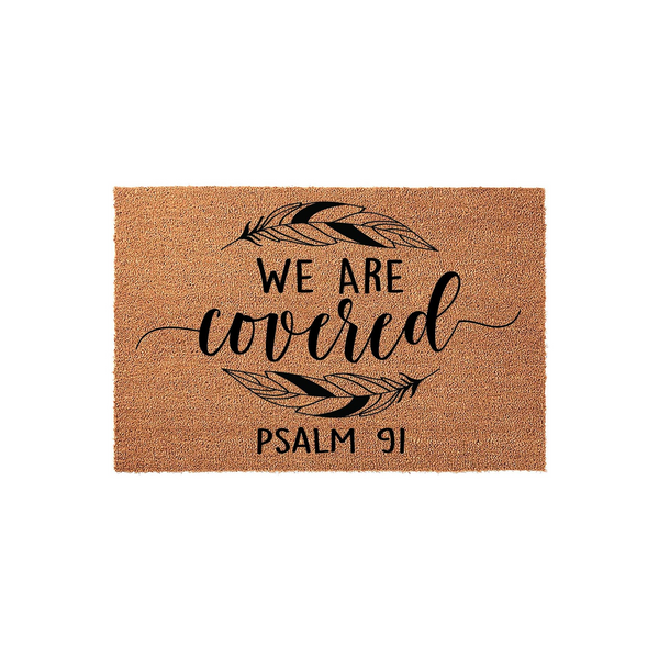 Psalm 91 We Are Covered coir doormat featuring a natural tan fiber texture with black printed text and two stylized feathers, creating a welcoming and faith-inspired entryway decor piece for your home on a clean white background.