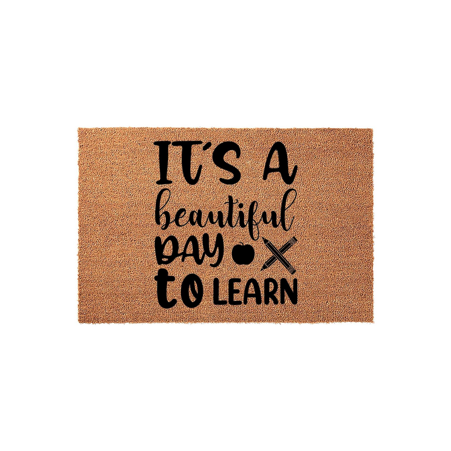 Teacher classroom doormat featuring the phrase It's a beautiful day to learn in black lettering, accented by a small apple and pencil icon on a natural brown coir fiber mat that adds a welcoming touch to any school or home office