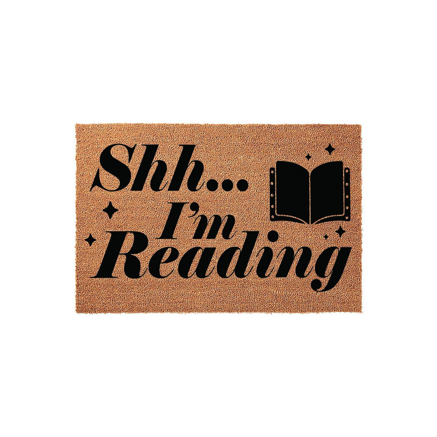 Shh I'm Reading coir doormat featuring bold black typography and a small open book icon with sparkles, set against a natural brown fiber background for a fun and welcoming entryway decor piece for any book lover's home.