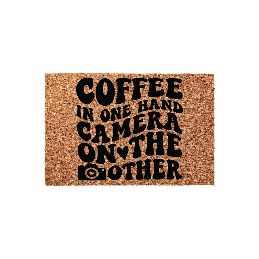 Photography Lover Coir Doormat featuring the text Coffee in one hand camera on the other in a bold, retro-style black font, set against a natural brown textured coir background with a small camera icon replacing the letter O.