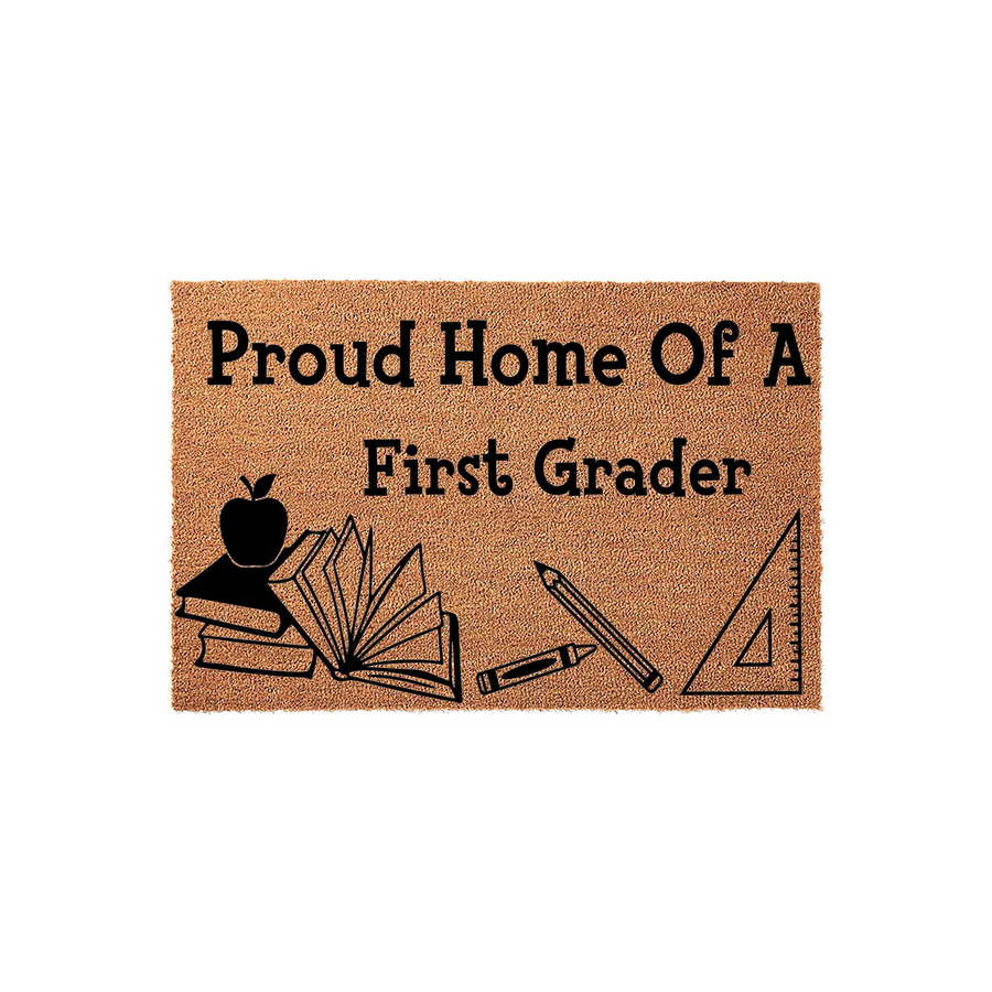 Proud Home Of A First Grader coir doormat featuring a natural tan fiber texture with black printed school supplies including an apple, a stack of books, a pencil, a crayon, and a ruler on a clean, isolated white studio background.