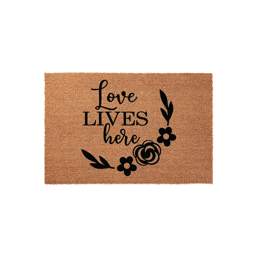 Love Lives Here coir doormat featuring a natural tan fiber texture and bold black lettering, accented by a decorative floral wreath design on the right side that adds a charming touch to any front porch or entryway home decor.