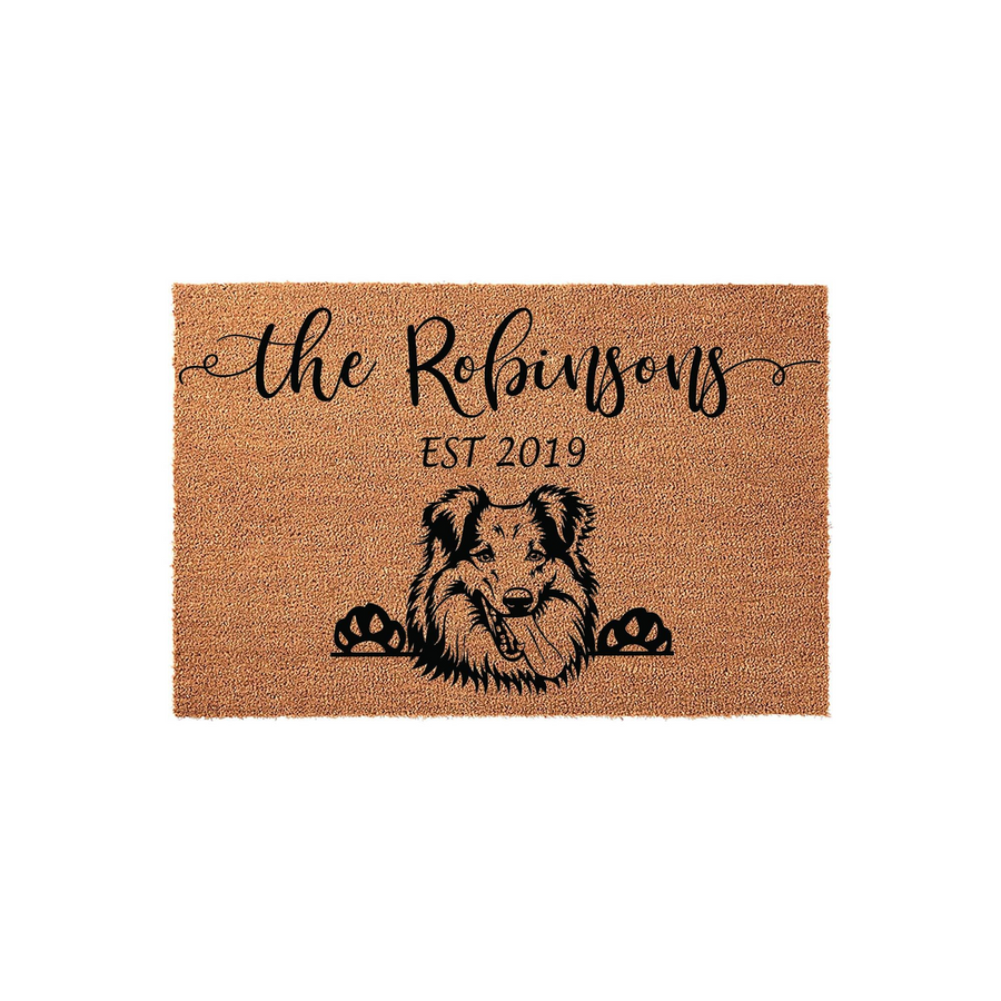 Personalized Collie dog doormat featuring a natural coir texture with a black printed illustration of a smiling Collie peeking over its paws, customized with a family name and established year on a clean white studio background.
