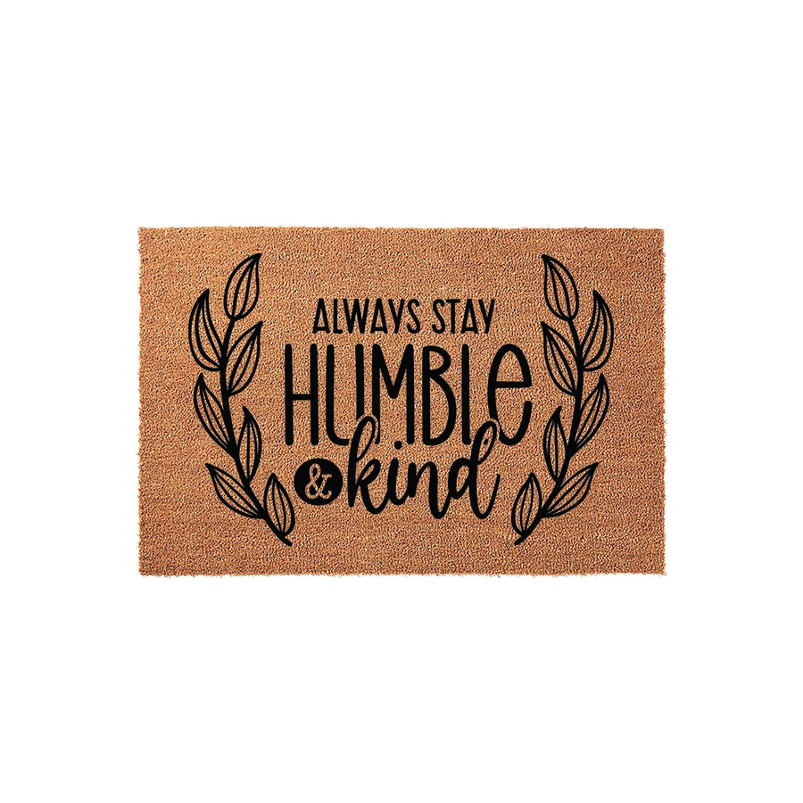 Always Stay Humble and Kind coir doormat featuring a natural brown fiber texture with black printed text and decorative leaf branches on the sides, creating a welcoming entryway decor piece for your front porch or home entrance.