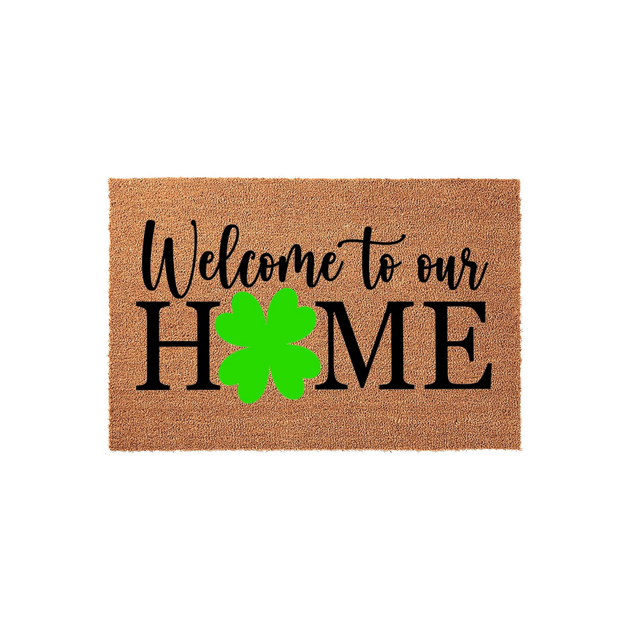 St. Patrick's Day Welcome to Our Home doormat made of natural coir fiber, featuring bold black lettering and a bright green four-leaf clover replacing the letter O in the word home, set against a clean white studio background.