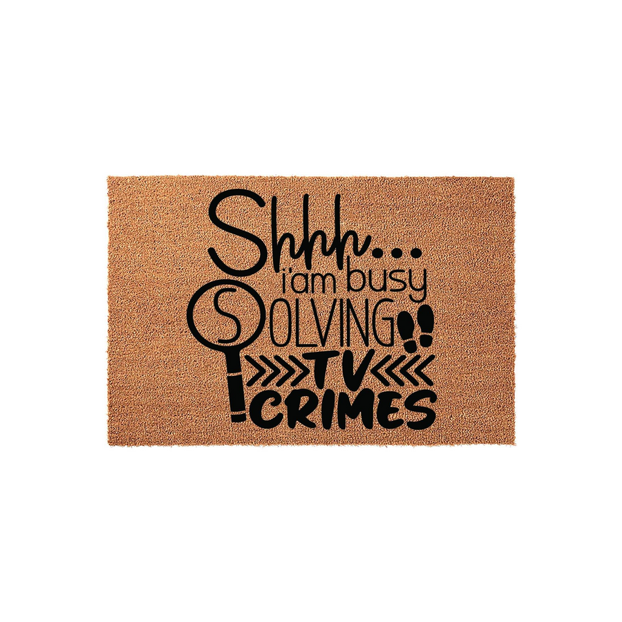 Shhh I am busy solving TV crimes doormat made of natural coir fiber with a black printed design featuring a magnifying glass icon and bold typography, perfect for a true crime fan who loves watching mystery shows at home.