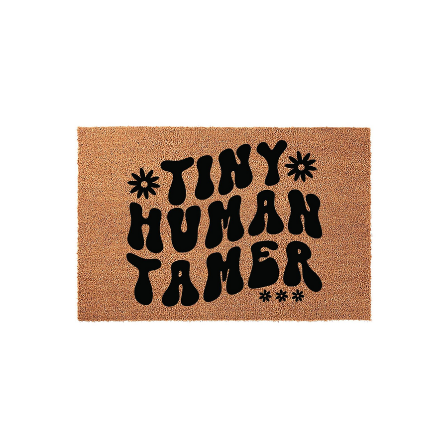 Tiny Human Tamer coir doormat featuring bold, retro-style black typography on a natural brown fiber background, accented with small flower icons to create a fun and welcoming entryway decor piece for parents of young children.