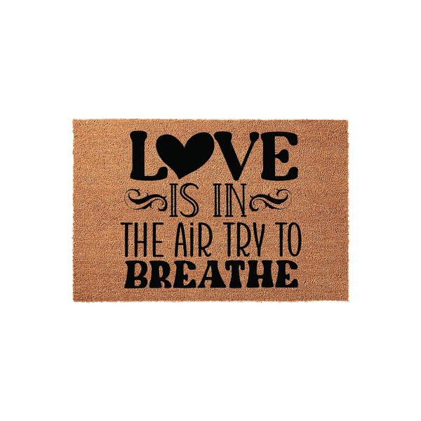 Love Is In The Air Try To Breathe Coir Doormat featuring a natural brown fiber texture with bold black lettering and a heart icon, creating a humorous and welcoming entrance decor piece for your front porch or home entryway.