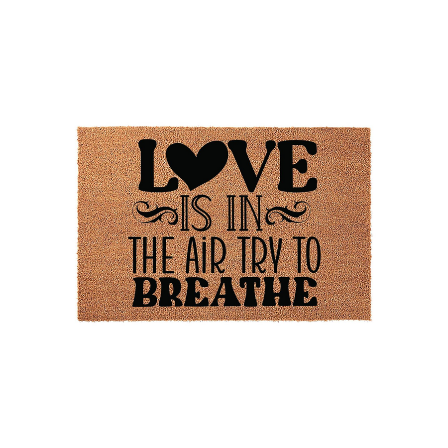Love Is In The Air Try To Breathe Coir Doormat featuring a natural brown fiber texture with bold black lettering and a heart icon, creating a humorous and welcoming entrance decor piece for your front porch or home entryway.