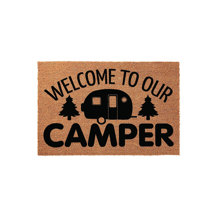 Welcome to Our Camper doormat featuring a natural coir texture with black printed text and a vintage travel trailer illustration flanked by two pine trees, creating a rustic outdoor aesthetic for any camping enthusiast's entryway.