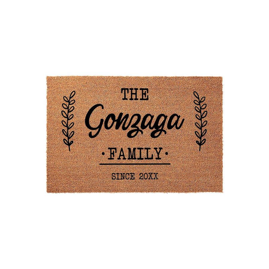 Personalized family name coir doormat featuring a rustic brown texture with black printed text that reads The Family and includes decorative leaf branches on both sides, creating a welcoming entrance for any home front porch
