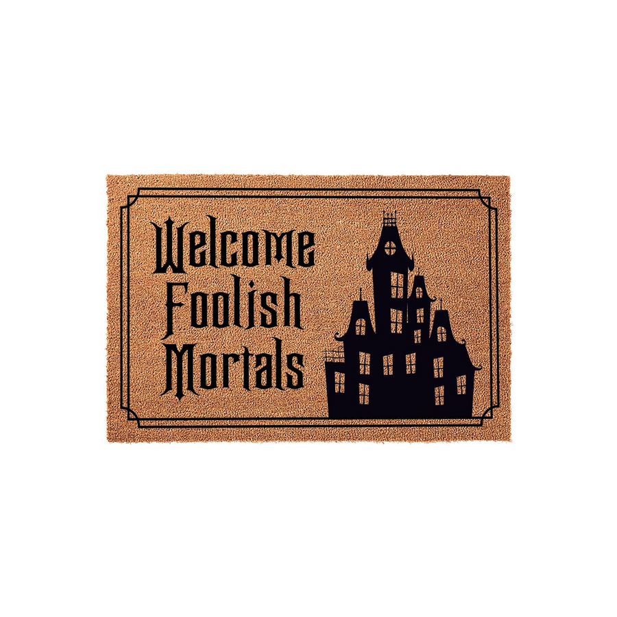Welcome Foolish Mortals Halloween doormat made of natural coir fiber, featuring a spooky haunted mansion silhouette printed in black ink against a textured brown background for a festive gothic entryway decor style.