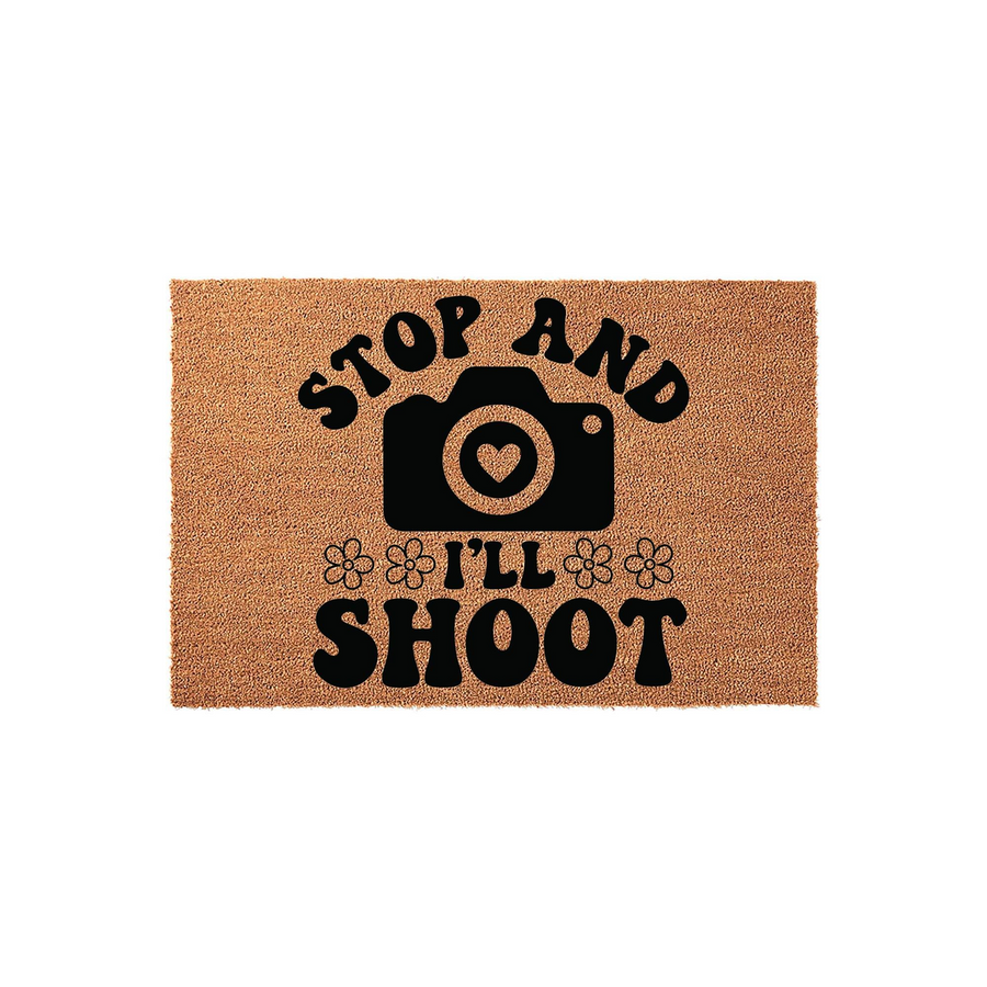 Photography lover coir doormat featuring the text Stop and I'll Shoot with a camera icon that has a heart lens, set against a natural brown fiber background with decorative flower accents for a fun entryway decor statement piece.
