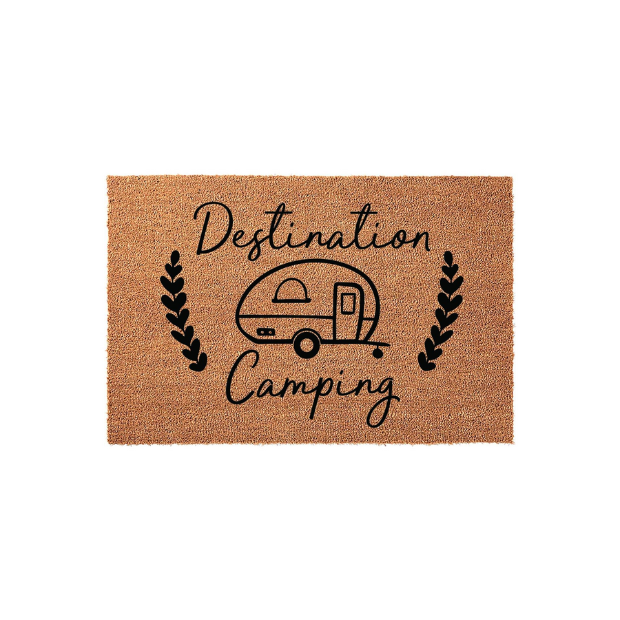 Destination Camping coir doormat featuring a black printed illustration of a vintage travel trailer surrounded by decorative leaf sprigs, set against a natural tan textured fiber background for a rustic outdoor home entrance