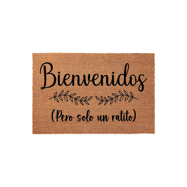 Funny Spanish Welcome Doormat featuring the text Bienvenidos Pero solo un ratito in black script and print fonts, centered on a natural brown coir fiber mat with a decorative leaf branch design for a humorous entryway home decor