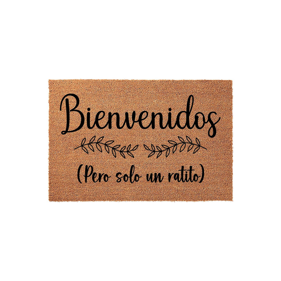 Funny Spanish Welcome Doormat featuring the text Bienvenidos Pero solo un ratito in black script and print fonts, centered on a natural brown coir fiber mat with a decorative leaf branch design for a humorous entryway home decor