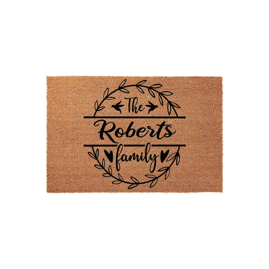 Personalized family name coir doormat featuring a black printed wreath design with birds and hearts, centered on a natural brown textured coconut fiber mat that provides a welcoming touch to any front porch or home entryway decor.