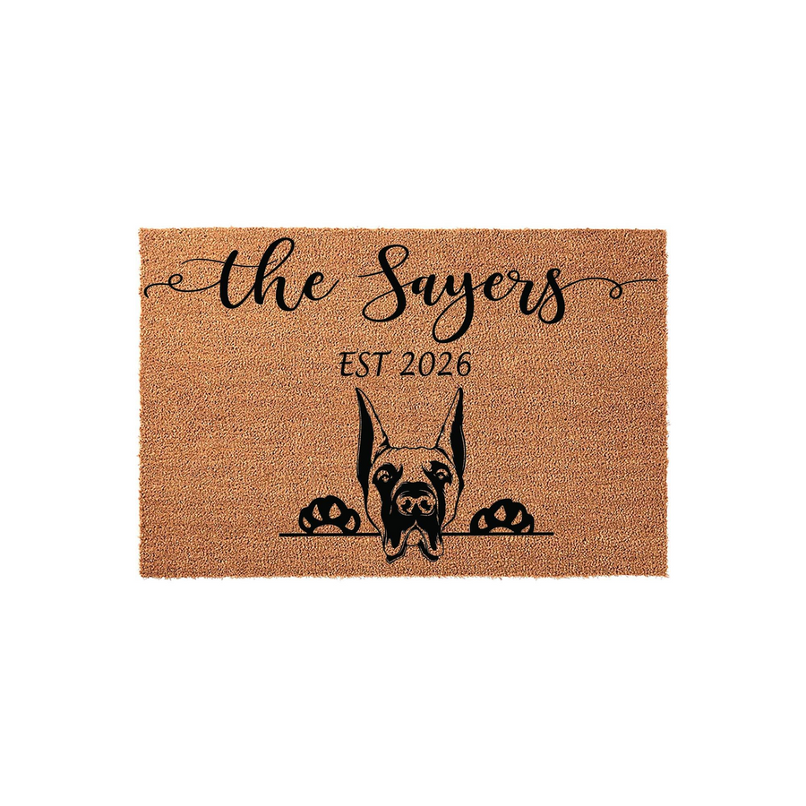 Personalized Doberman Pinscher doormat featuring a cute dog peeking over a line with custom family name text and established year, printed on a natural coir fiber mat against a clean white studio background for a welcoming home