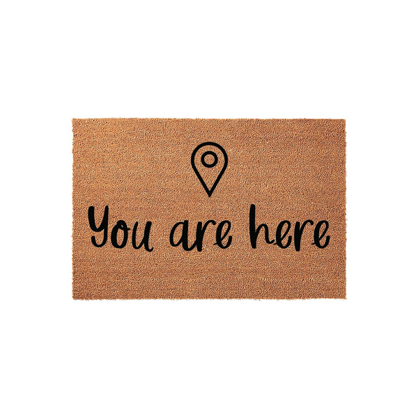 You are here coir doormat featuring a minimalist black map location pin icon centered above the playful cursive text, set against a natural brown textured fiber background for a modern and welcoming front porch entrance decor.