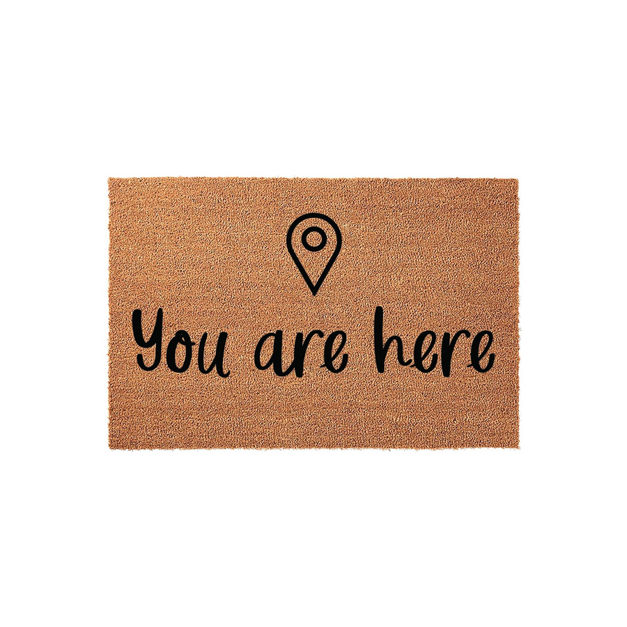 You are here coir doormat featuring a minimalist black map location pin icon centered above the playful cursive text, set against a natural brown textured fiber background for a modern and welcoming front porch entrance decor.