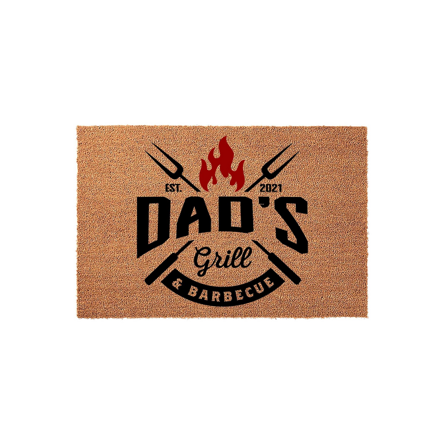 Dad's Grill and Barbecue coir doormat featuring a bold black and red design with crossed grilling forks, a flame icon, and the text Dad's Grill and Barbecue established in 2021, set against a plain white studio background.