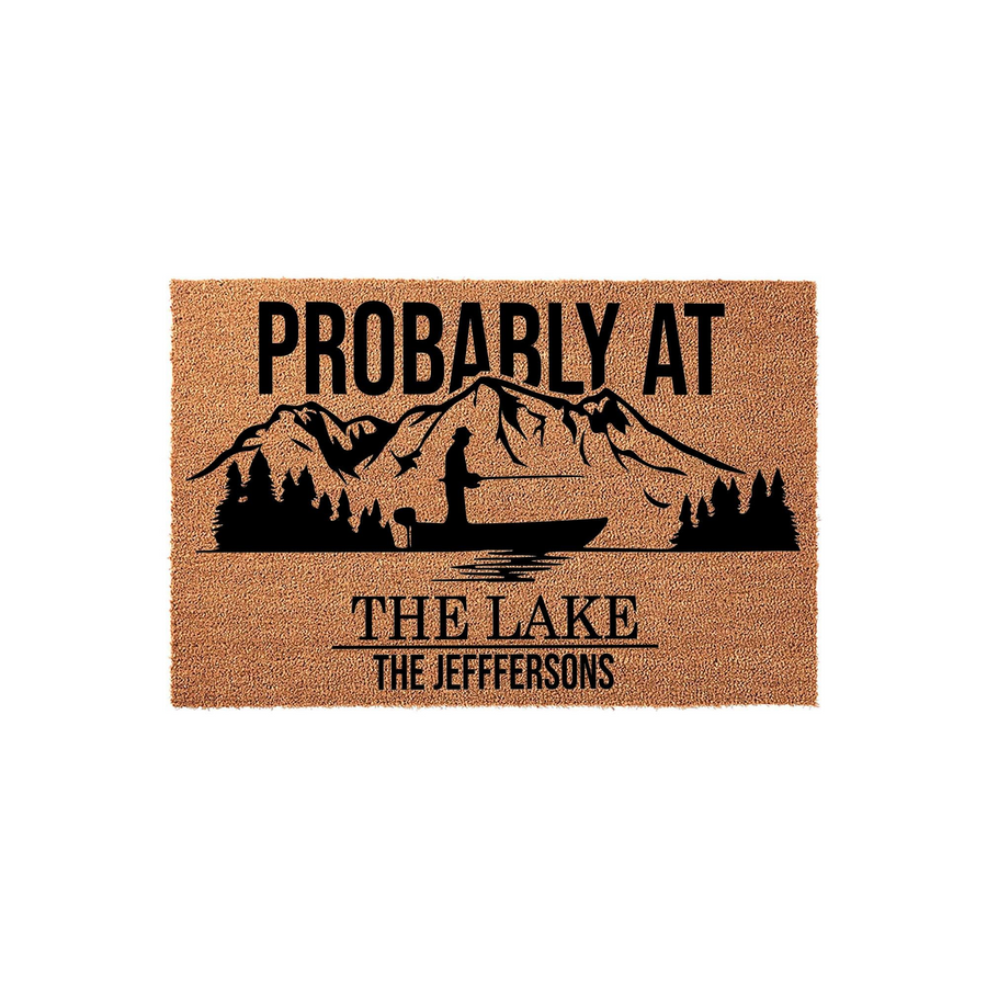 Personalized Lake House Doormat featuring a rustic coir texture with a black graphic of a fisherman in a boat on a lake with mountains, displaying the text Probably At The Lake and a space for a custom family name on a white