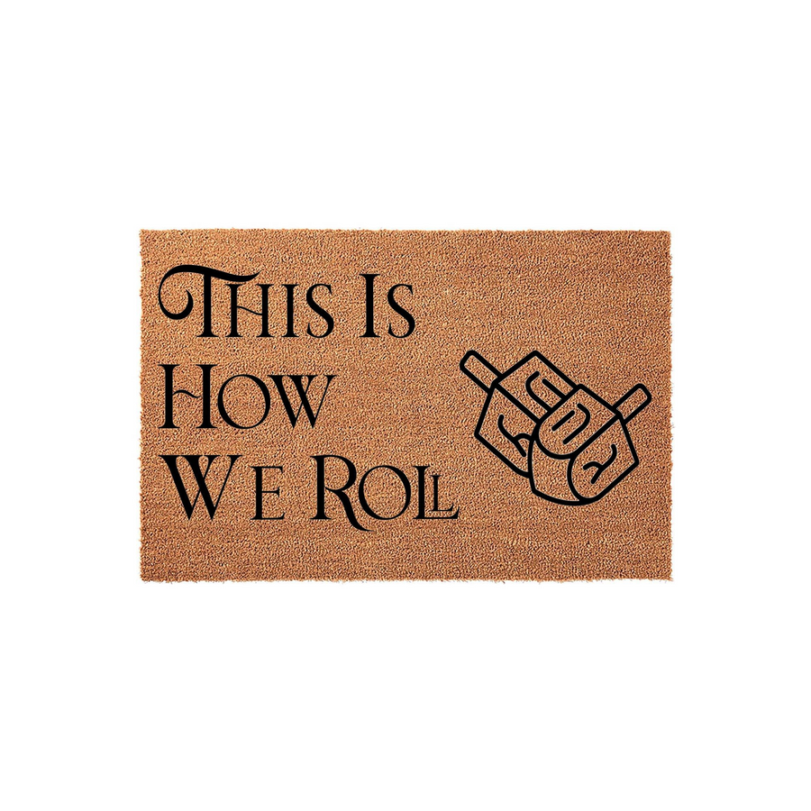 Hanukkah Dreidel Welcome Doormat featuring a natural coir texture with black text that reads This Is How We Roll, accompanied by a graphic illustration of a spinning dreidel toy for a festive holiday home entryway decoration.